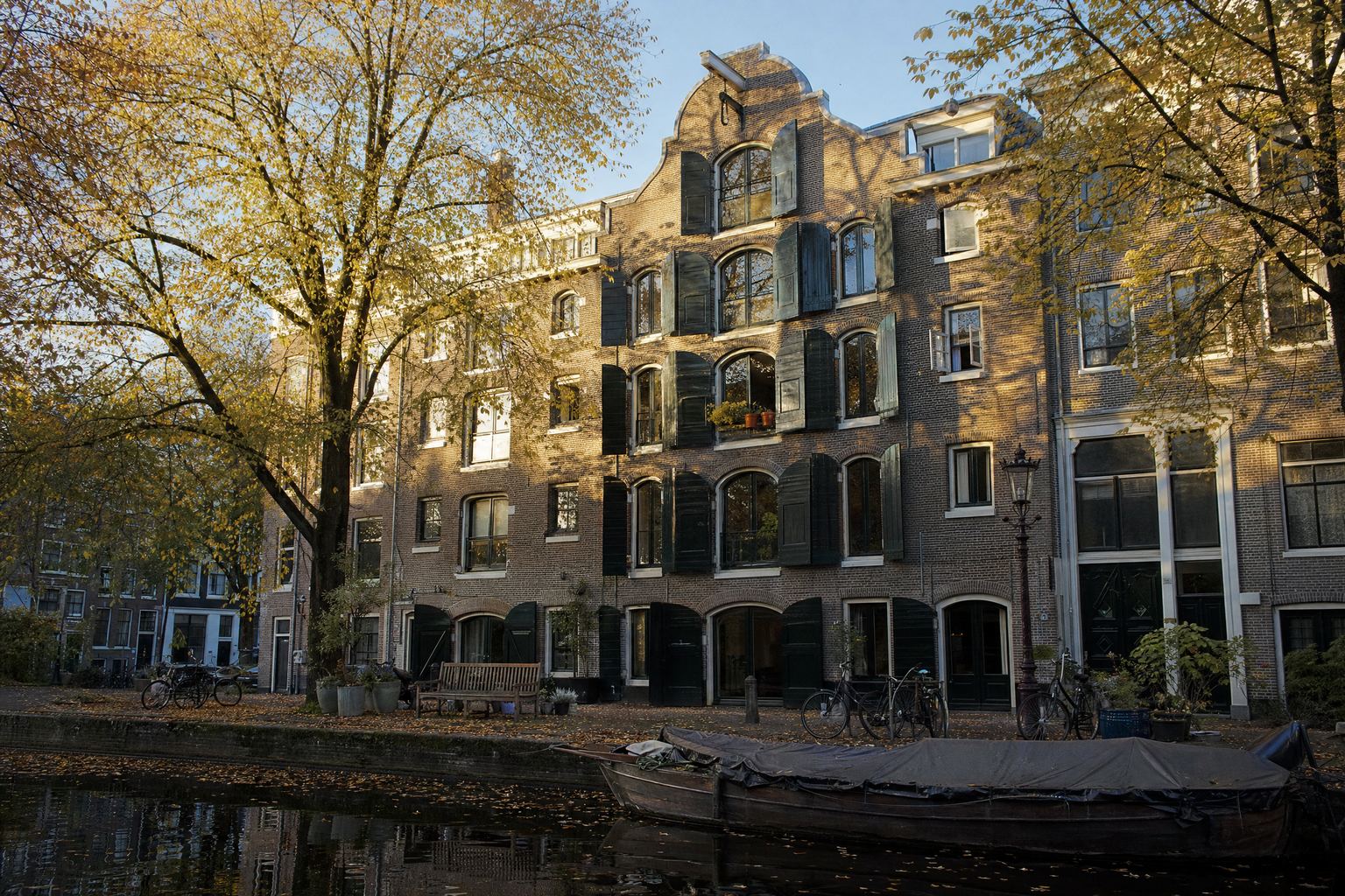 Sfeerbeeld van een pakhuis met groene luiken aan een gracht in de herfstzon